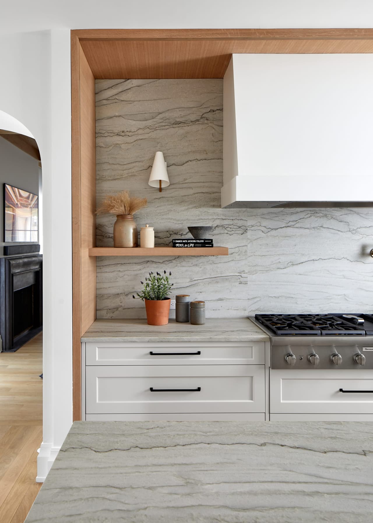 Range alcove framed in white oak with a full-height quartzite slab, a white plaster hood and a floating oak shelf