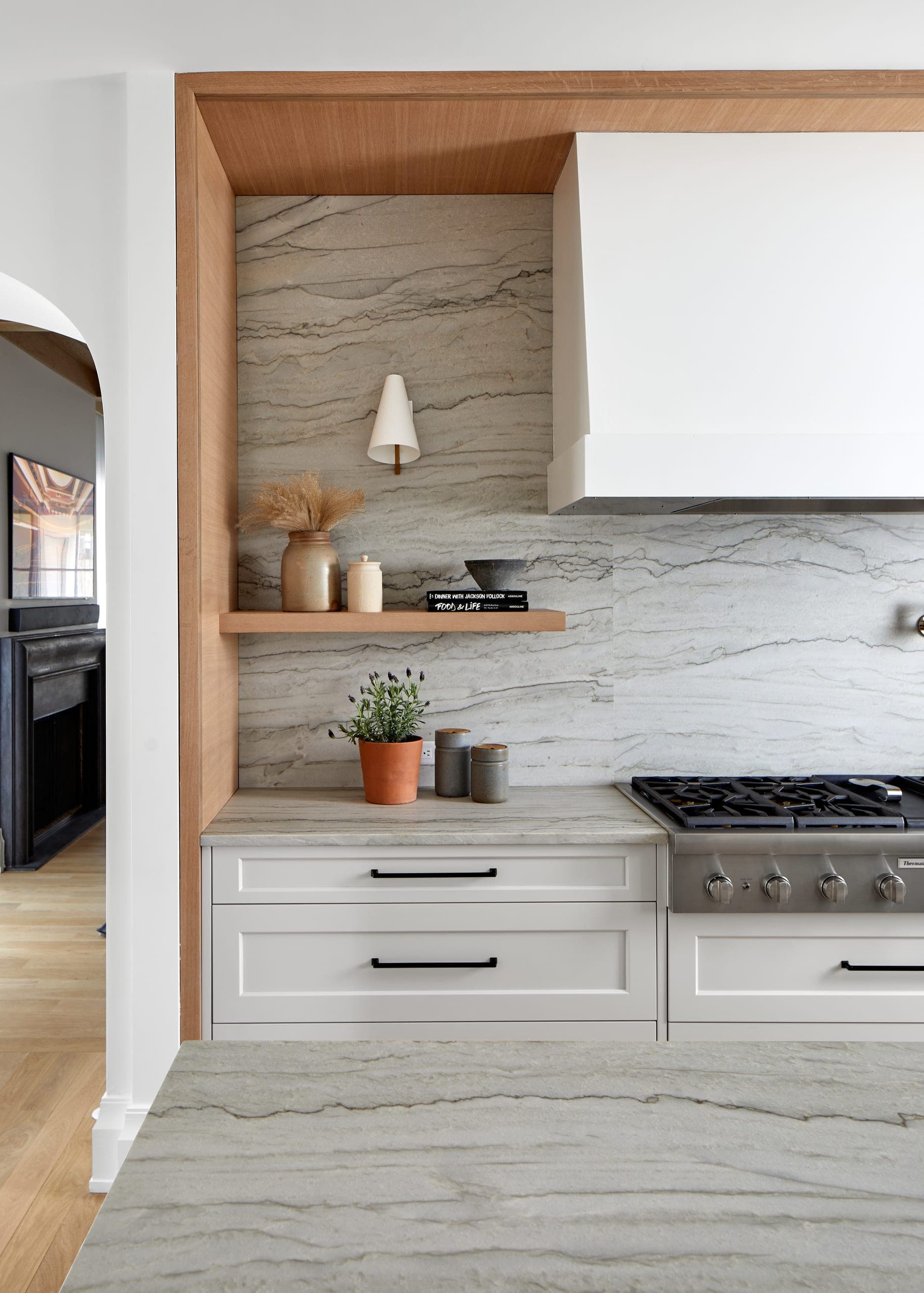 Range alcove framed in white oak with a full-height quartzite slab backsplash, a white plaster hood and a floating oak shelf