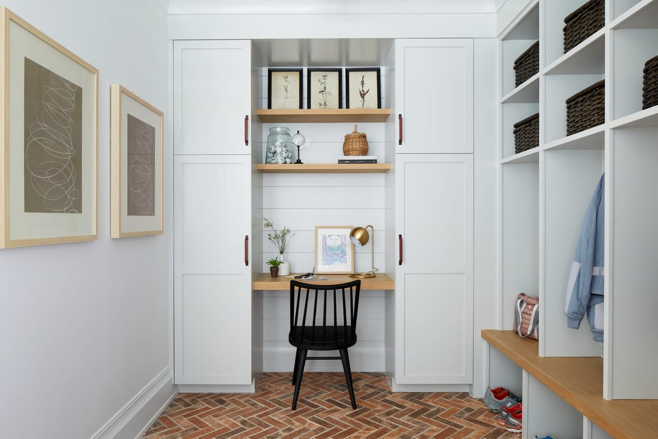 Mudroom with white built-in lockers, a small desk nook and a herringbone brick floor
