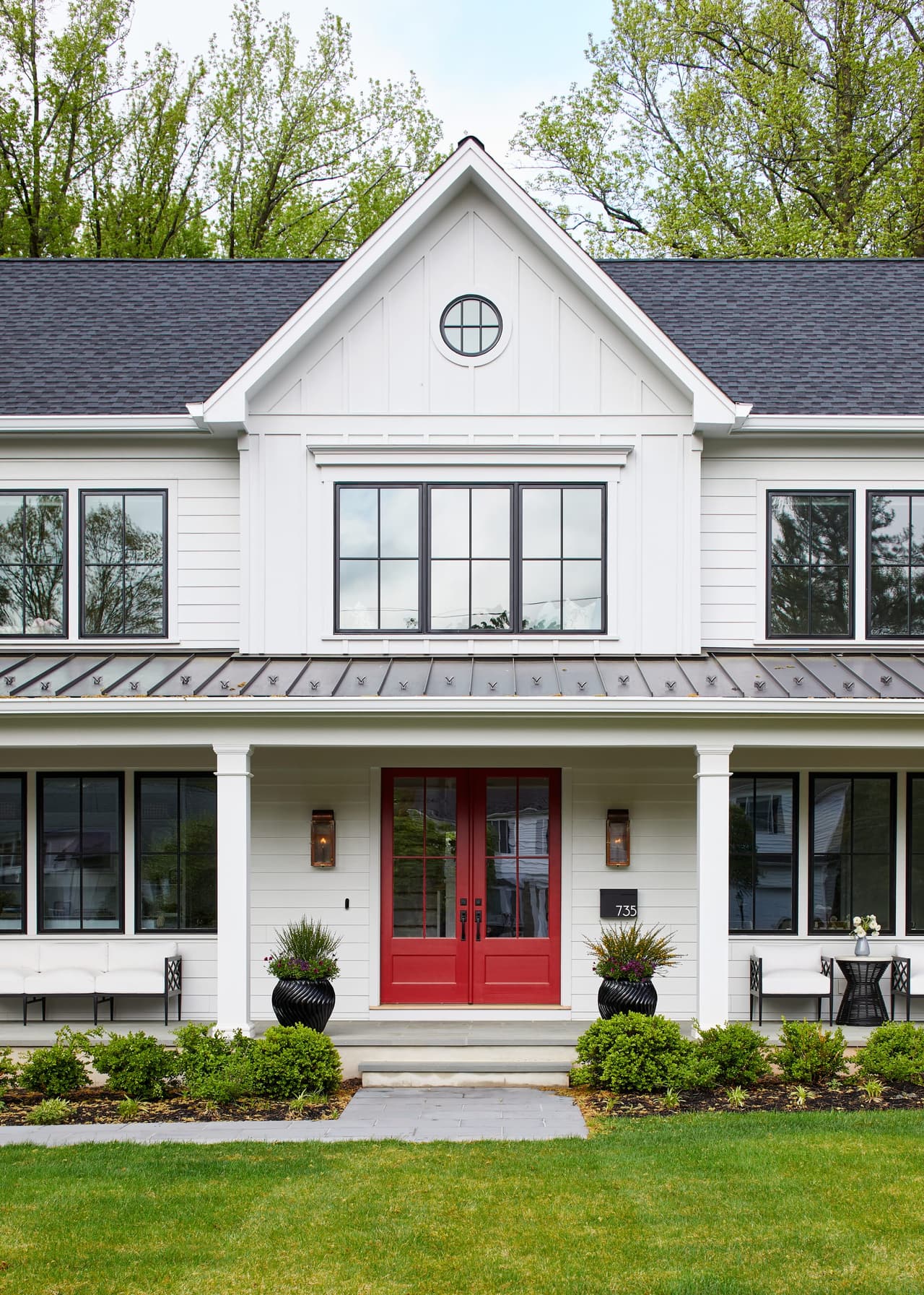 White modern farmhouse with black windows, a red front door and a gabled dormer above the porch