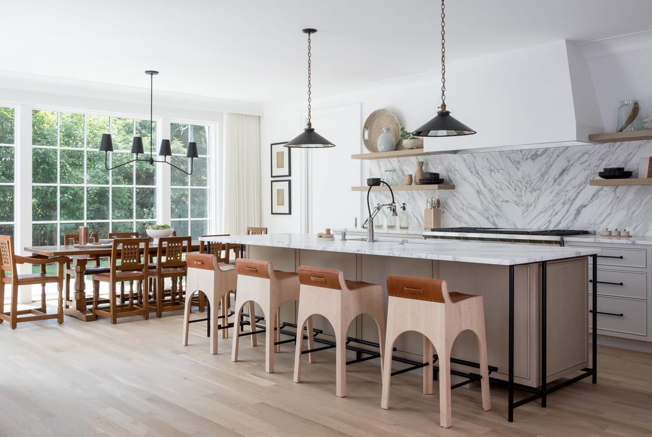 Kitchen of a Westfield, NJ new-construction home, with a long island running into a table, white counter stools and a marble slab behind the range