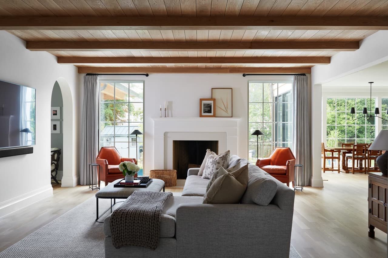 Open-concept family room in a Westfield, NJ custom home, with a planked wood ceiling on exposed beams, an arched cased opening and a fireplace between sliding glass doors, built by Michael Robert Construction