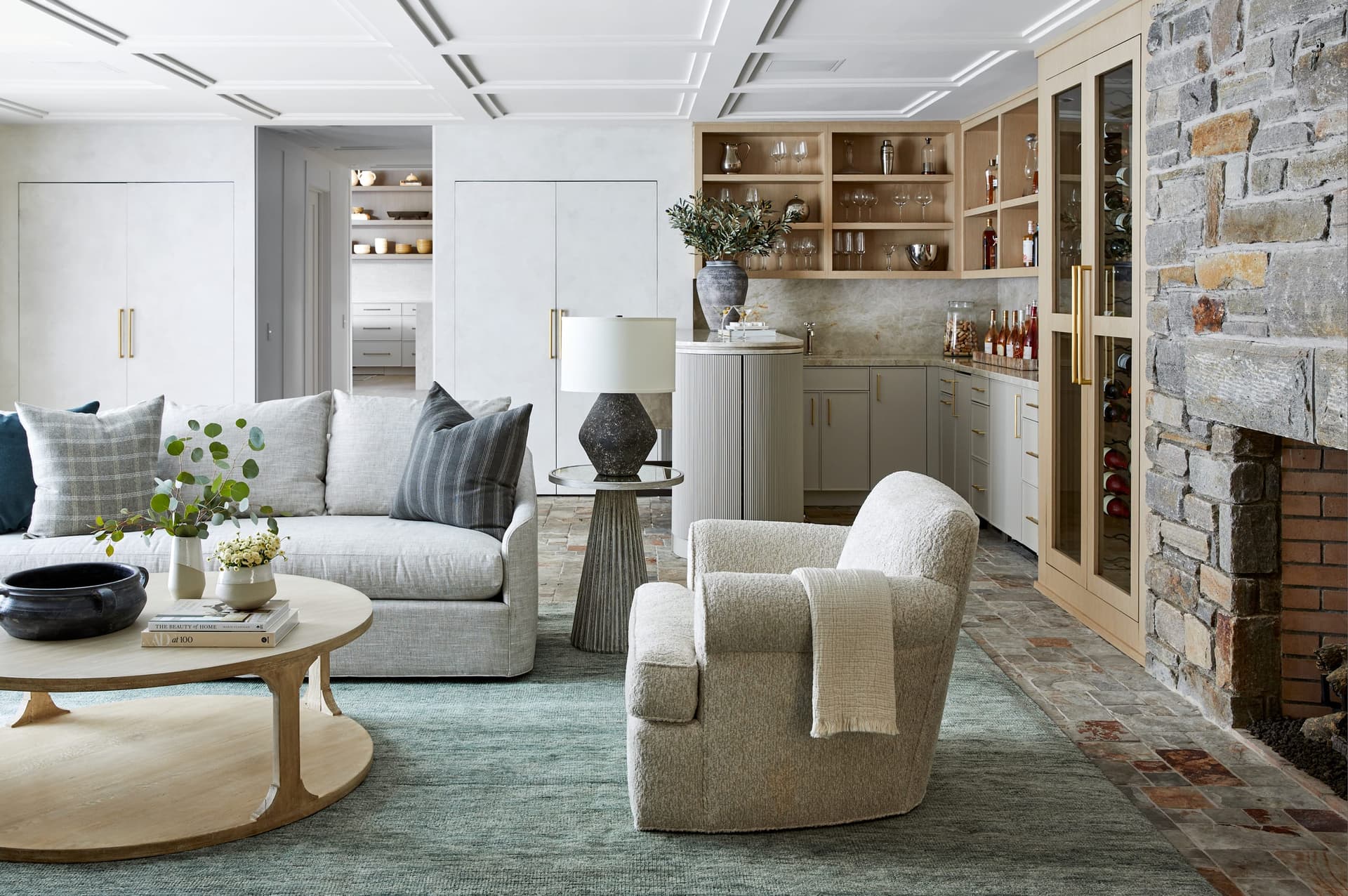 Family room of a Westfield, NJ home renovation, with a stone fireplace wall, swivel chairs on a teal rug and a built-in bar in oak at the far end