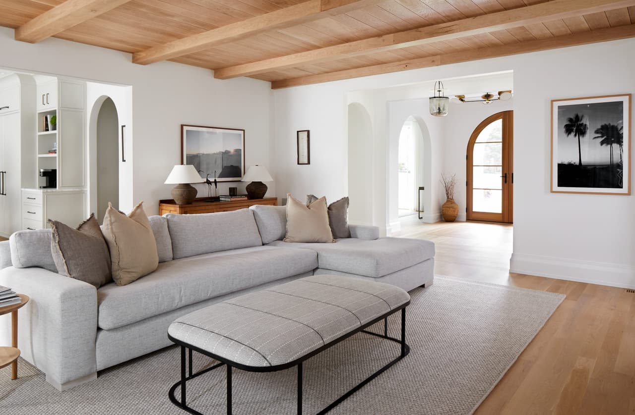 Sitting room in a Westfield, NJ custom home under a vaulted plank ceiling on exposed beams, with arched cased openings and a low sectional on a pale rug, built by Michael Robert Construction