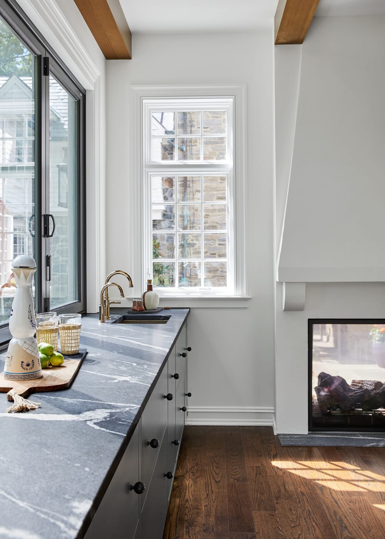 Soapstone bar counter running to the window in a Westfield, NJ home renovation, with navy cabinetry below and a see-through fireplace at the end