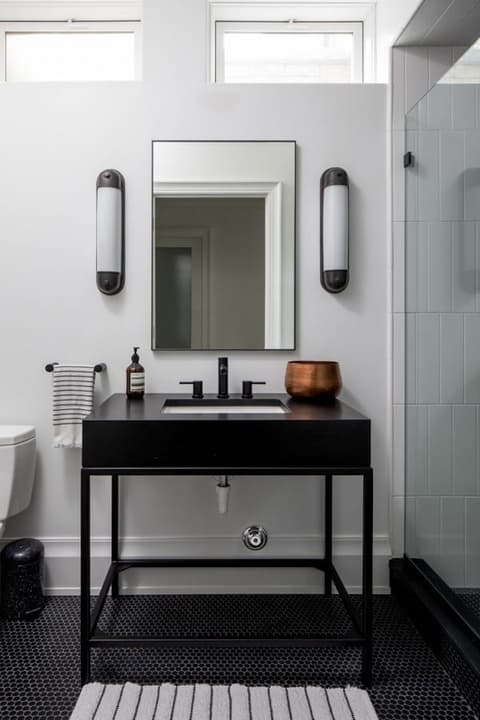 Basement bathroom in a Westfield, NJ home, with a black metal console basin, tube sconces either side of the mirror and a striped tile floor