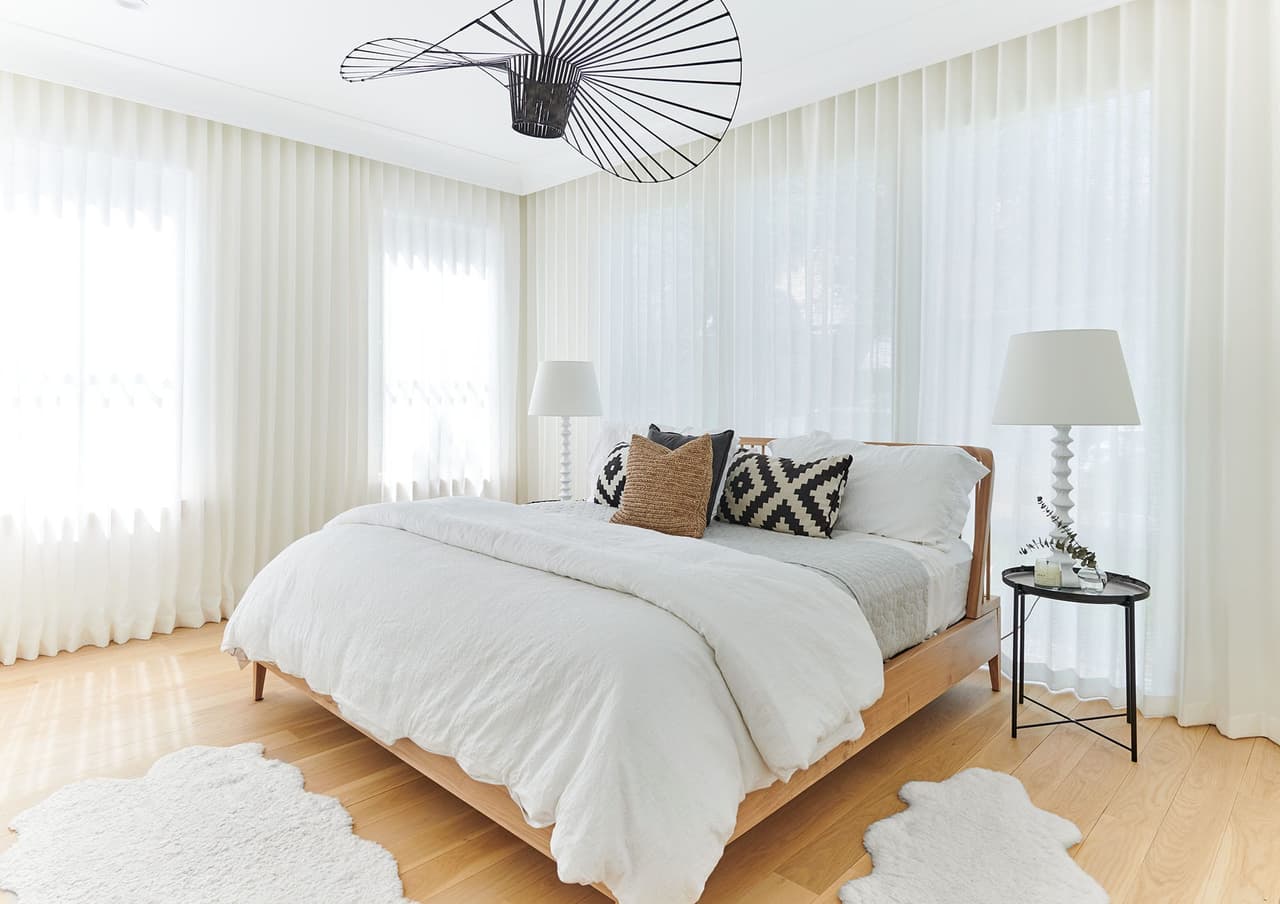 Bedroom in the Mroz family home in Westfield, NJ, with sheer curtains across two walls, a hide rug and a spoked pendant on the planked ceiling