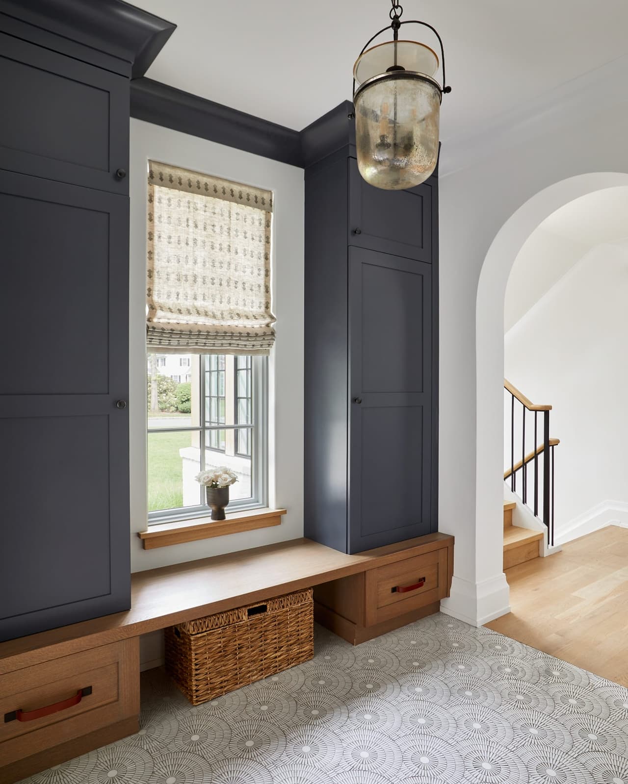 Mudroom with navy custom cabinetry in a Westfield, NJ new home, with a window seat over basket drawers, a Roman shade and a patterned tile floor
