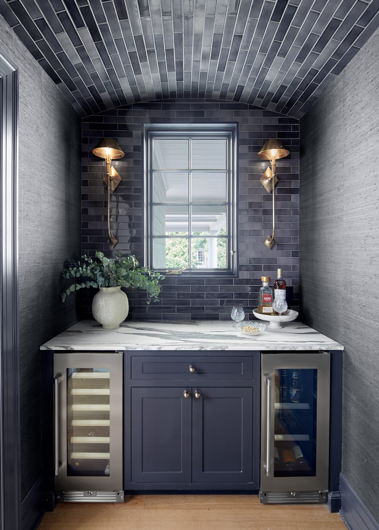Navy butler's pantry in a historic Westfield, NJ home, under a dark-tiled vaulted ceiling, with brass sconces lit either side of the window and wine refrigeration below