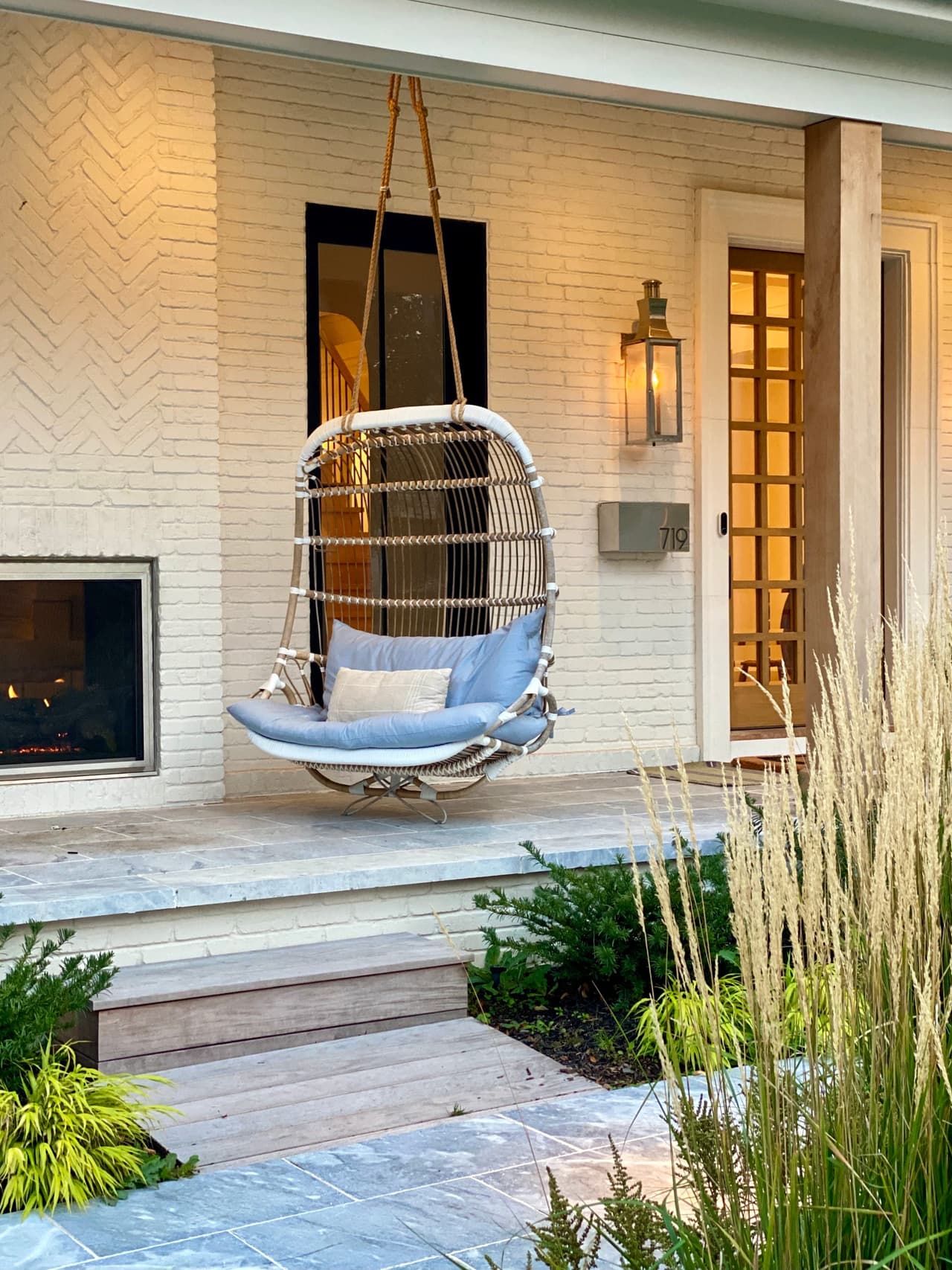 Porch of a Westfield, NJ new-construction home, with a hanging rattan egg chair, a herringbone brick chimney breast and a lantern beside the door