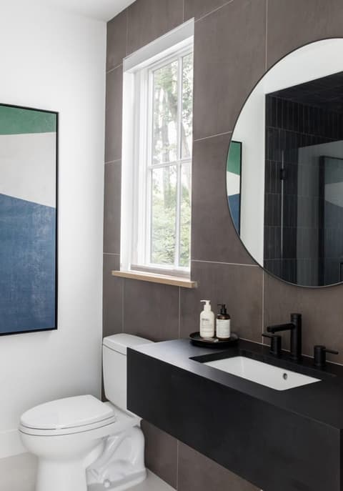 Powder room with a floating dark vanity, a round mirror and large-format tile to the ceiling