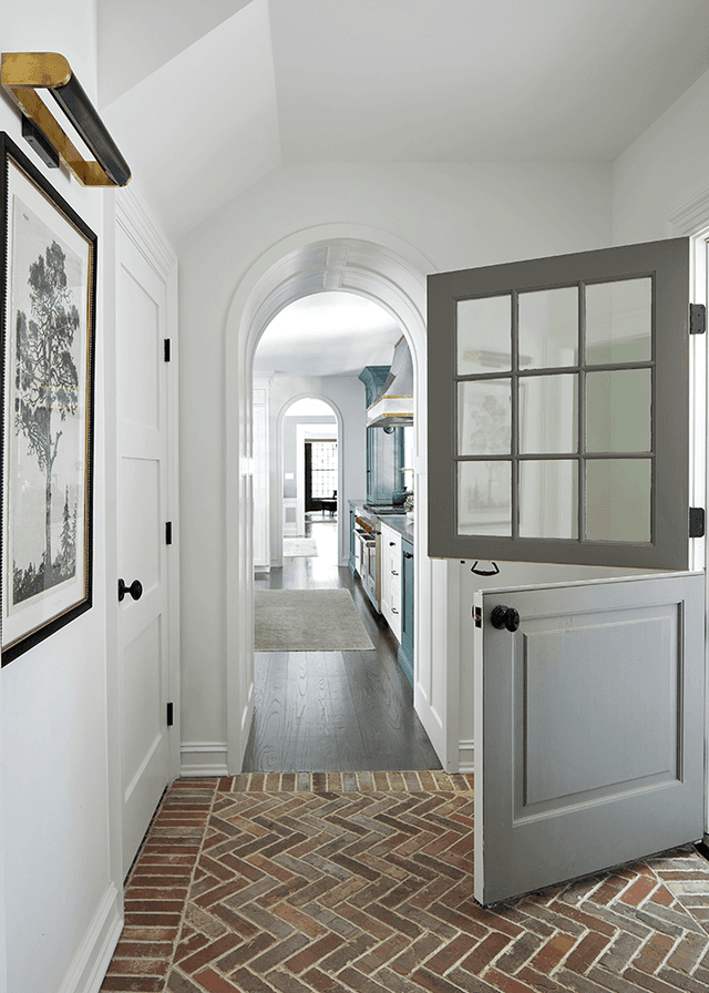 Dutch door standing half open onto the herringbone brick entry of a Westfield, NJ home renovation, with an arched opening through to the kitchen