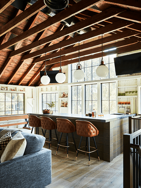 Bar and leather counter stools under the exposed rafters of a Westfield, NJ historic barn renovation, with globe pendants hung from the collar ties