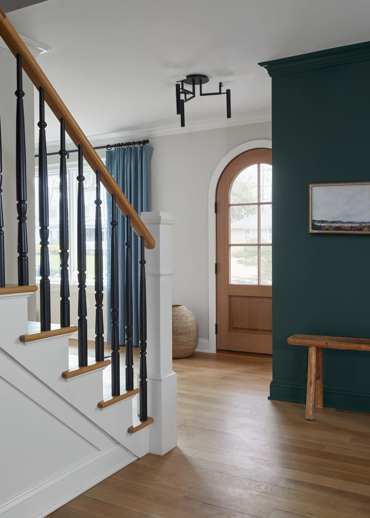 Entry of a Westfield, NJ whole-home renovation, with a deep green wall, an arched door, a white stair with a black rail and a wood bench