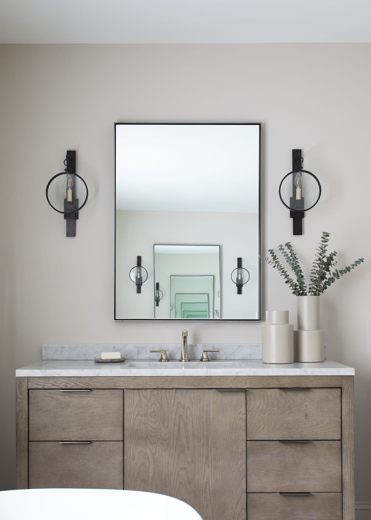 Oak vanity with a stone top, black sconces and a thin-framed mirror in a Westfield, NJ primary bathroom renovation