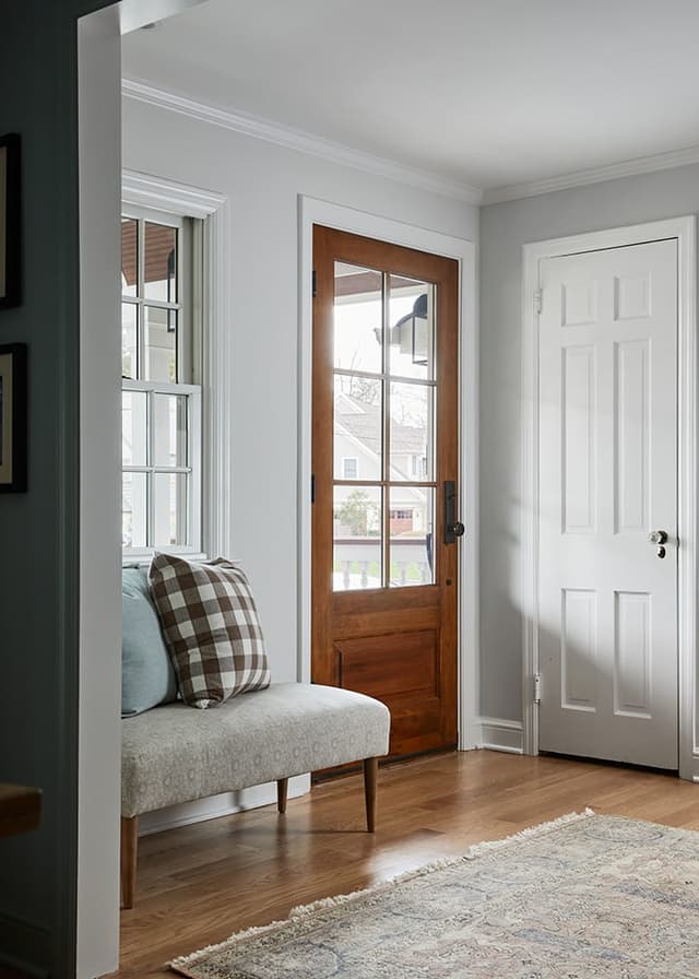 Entry of a Westfield, NJ renovation with a glazed wood front door, an upholstered bench and a runner on wide-plank floors
