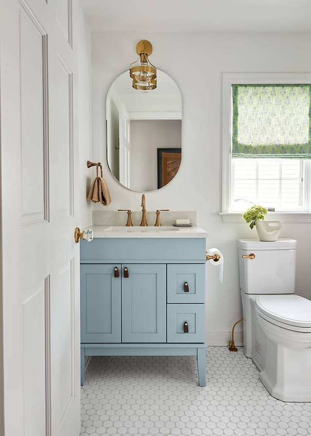 Guest bathroom in a Westfield, NJ renovation with a pale blue vanity, brass tap and arched mirror under a globe pendant