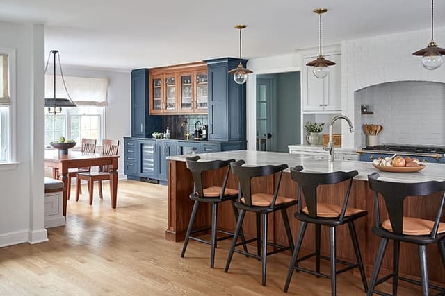 Walnut and white kitchen in a Westfield, NJ home, with a plaster hood over the range, black counter stools at the island and a navy built-in bar beyond