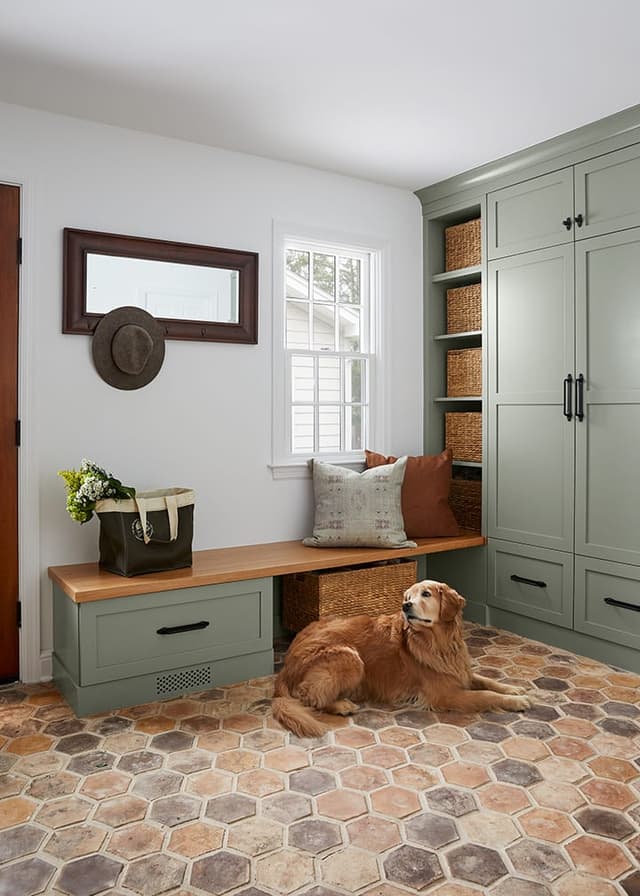 Golden retriever lying on the hexagonal tile floor of a Westfield, NJ mudroom renovation, with sage green cabinetry and a walnut bench under the window