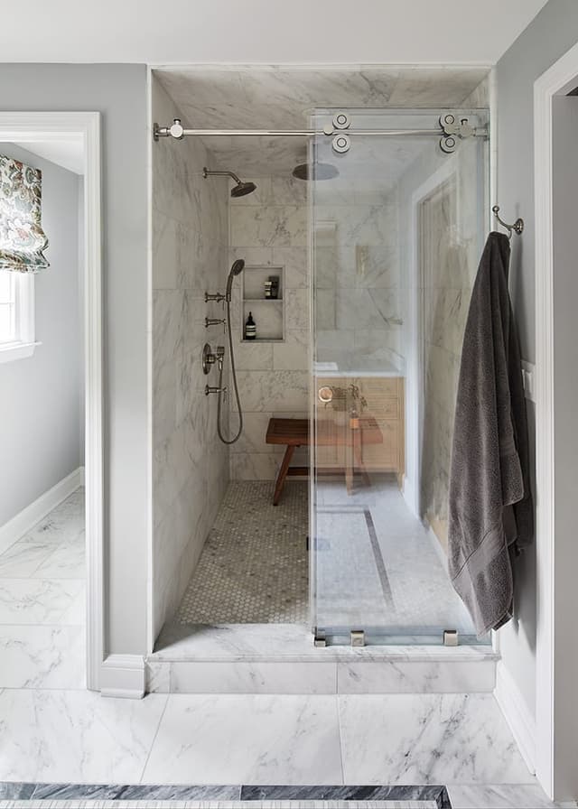 Marble-lined shower with a sliding glass door and a built-in bench in a Westfield, NJ primary bathroom renovation