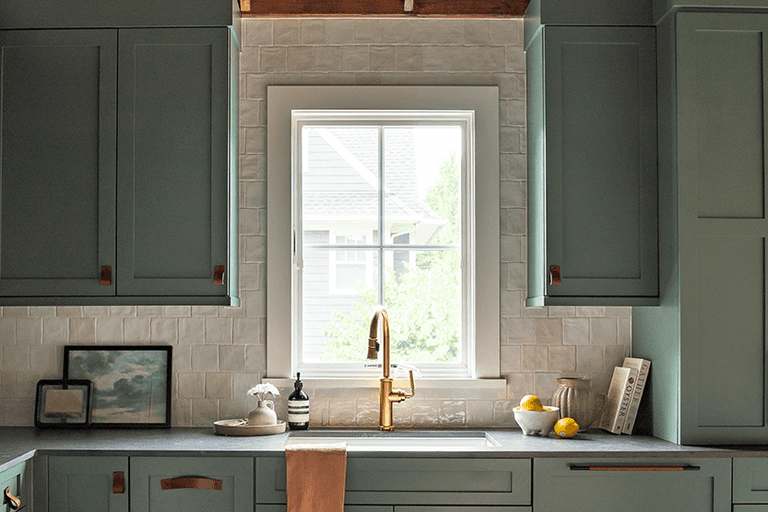 Sage custom cabinetry and zellige tile around a window and brass bridge tap in a Westfield, NJ barn renovation kitchen
