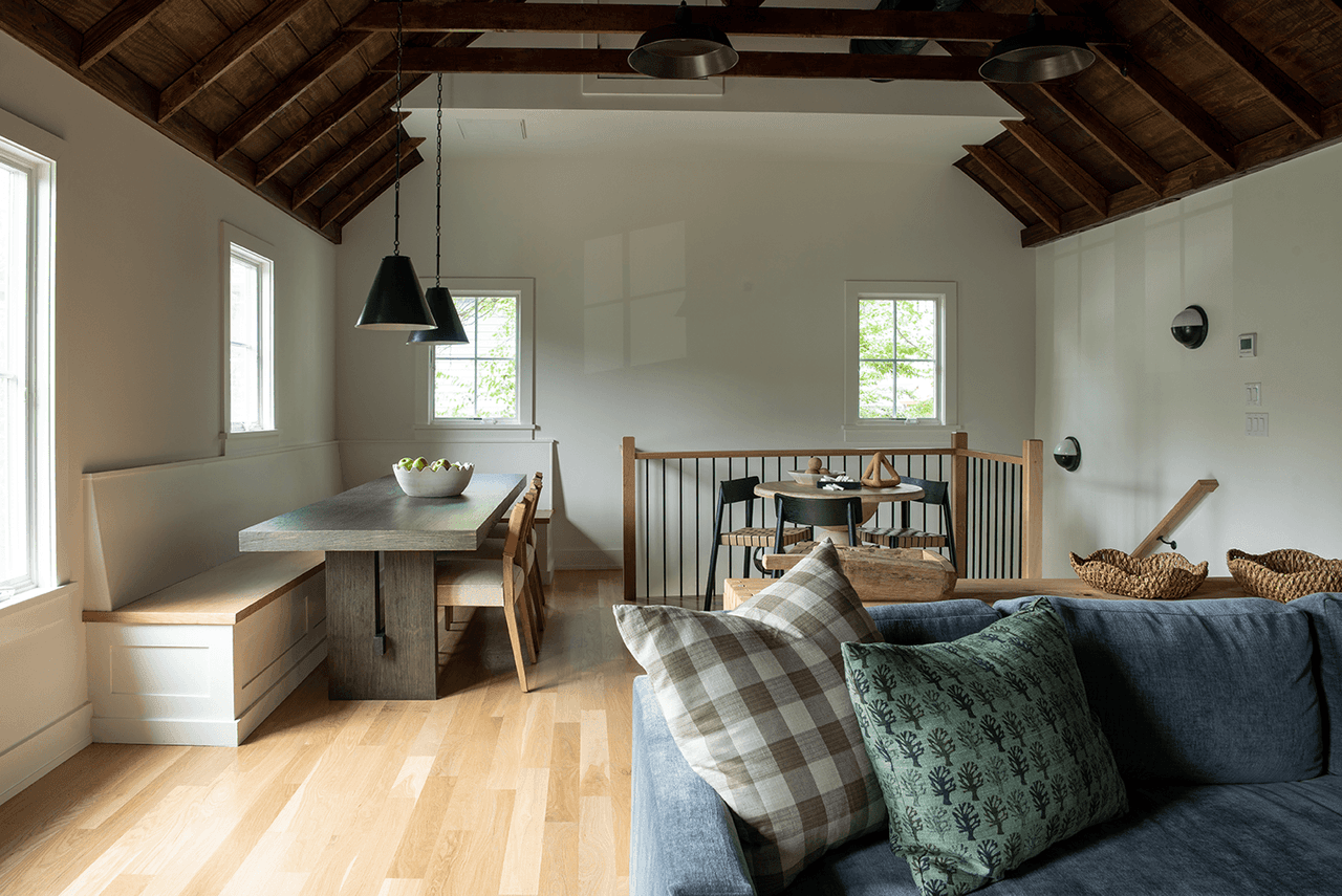 Dining and game table under the exposed rafters of a Westfield, NJ barn renovation, with a window banquette and a wall-mounted sconce