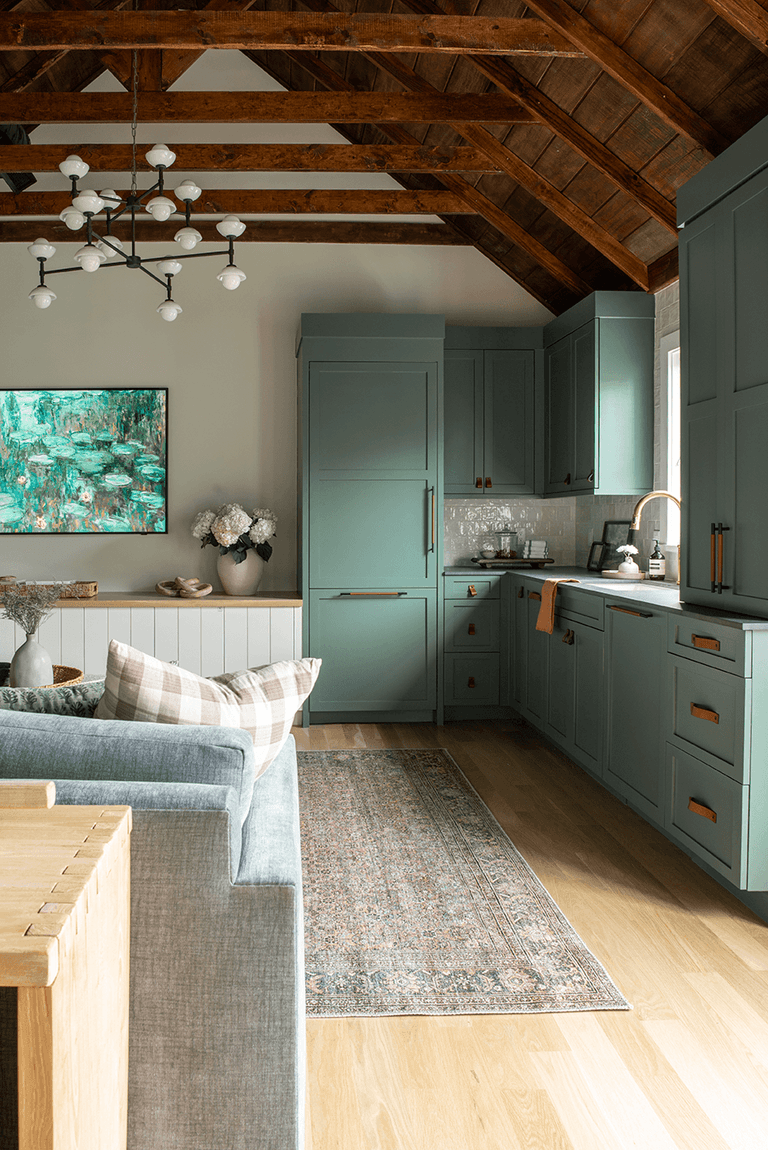 Kitchenette in a Westfield, NJ barn renovation, with sage green custom cabinets under the exposed rafters and a branching brass chandelier overhead