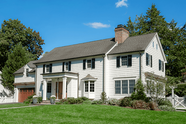 Angled view of a Westfield, NJ exterior renovation from the lawn, with white clapboard, black shutters, cedar accents and an attached garage, by Michael Robert Construction