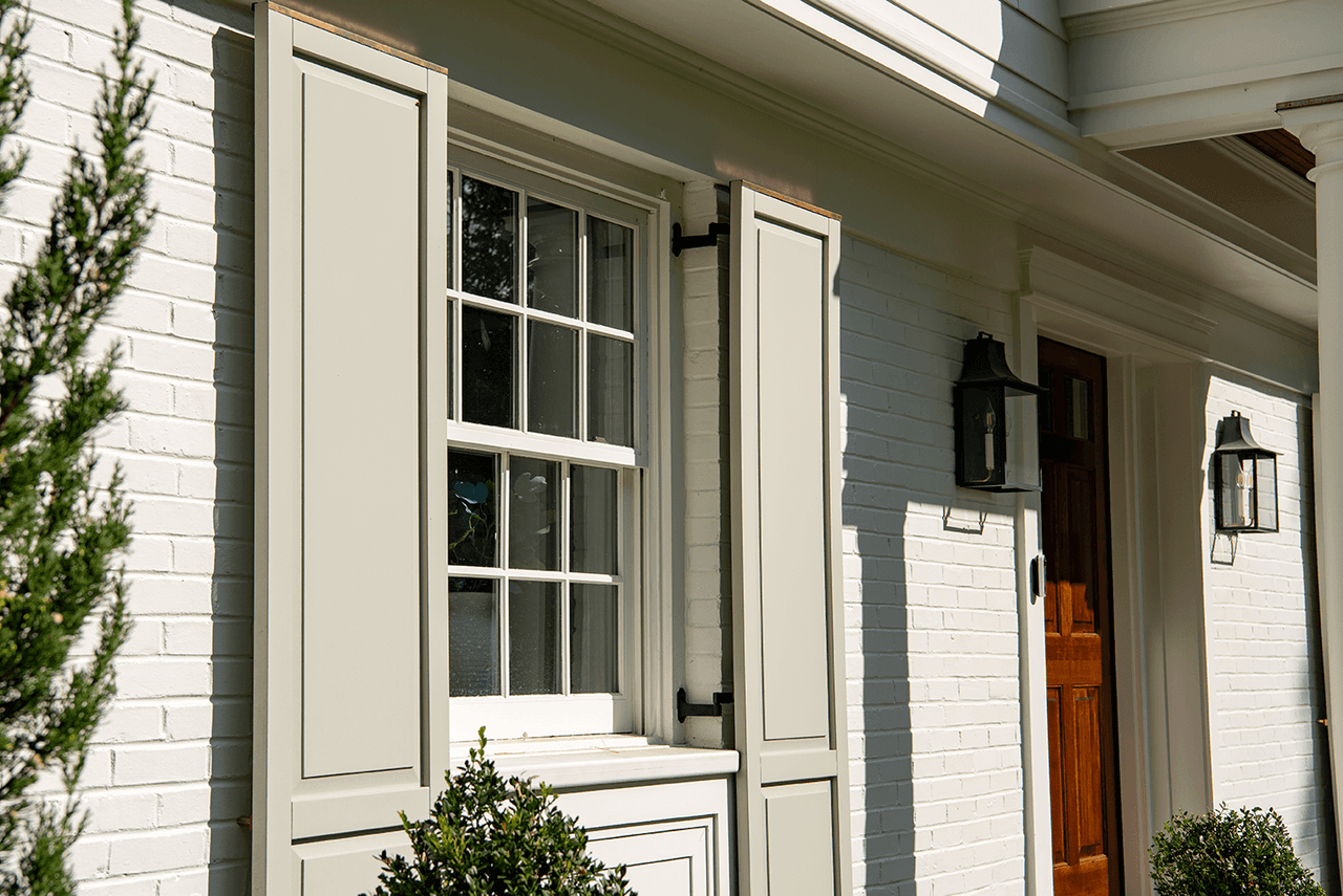 Custom louvered shutters and a lantern beside the door of a Summit, NJ exterior renovation, seen at an angle along the painted brick