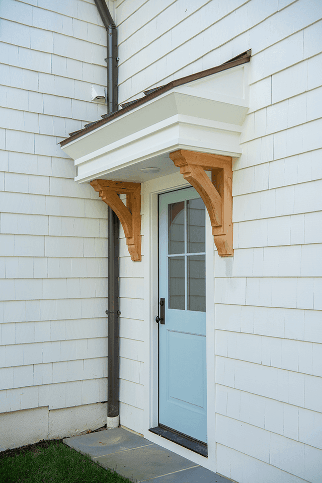 Pale blue side door under a cedar-bracketed hood in the white clapboard wall of a Westfield, NJ home renovation by Michael Robert Construction