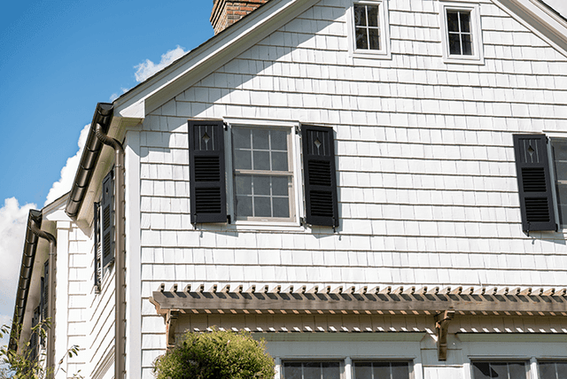 Cedar pergola bracket set against shingled siding beside black shutters on a Westfield, NJ exterior renovation by Michael Robert Construction