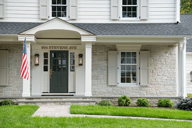Columned entry portico and stone veneer on the front of a Westfield, NJ exterior remodel, with a green front door and dark shutters
