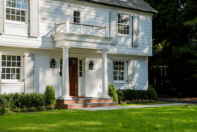 Columned portico and wood front door on a Summit, NJ exterior renovation, with a balustraded roof deck above and brick steps down to the lawn