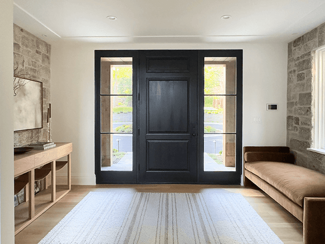 Entry of a Mendham, NJ home with a black front door between sidelights, an exposed stone wall and a leather bench along the window