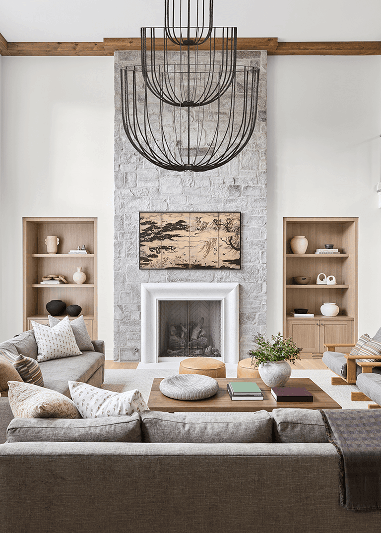 Stone chimney breast rising to the ceiling in the family room of a Mendham, NJ home renovation, flanked by oak shelving under a wire-frame chandelier