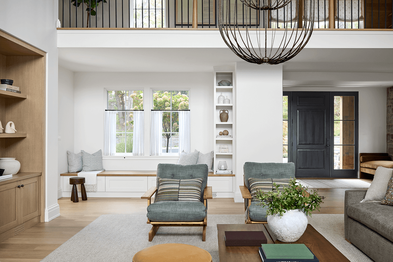 Window seat and built-in shelving at the end of the family room in a Mendham, NJ home renovation, with two green lounge chairs on a pale rug