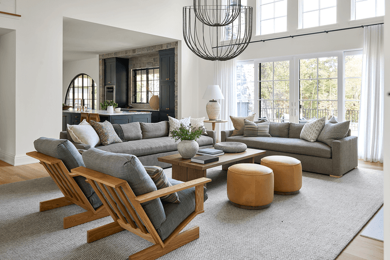 Family room of a Mendham, NJ home renovation, with a wire-frame chandelier, two sectionals and low wooden lounge chairs on a pale rug