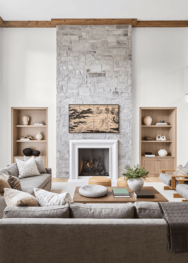 Family room with a stacked stone chimney breast, a marble fireplace surround and oak built-in shelves either side, under a beam across the ceiling