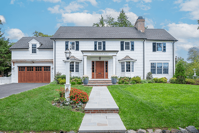 Front of a white shingled Westfield, NJ exterior renovation from the walk, with black shutters, a cedar front door and a wood garage door on the wing