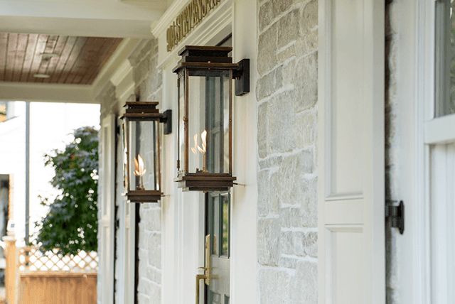 Two lit gas lanterns mounted on the stone and trim of a Westfield, NJ exterior renovation, under a stained porch ceiling