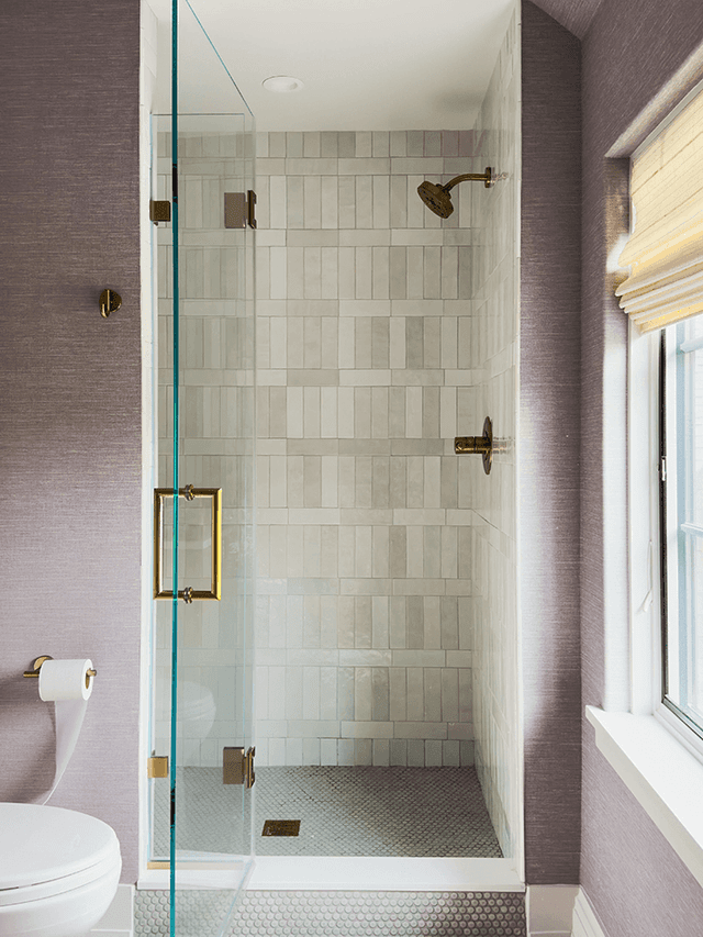 Children's bathroom in a Mendham, NJ home, with a zellige-tiled shower behind brass-framed glass, lilac grasscloth walls and a penny tile floor