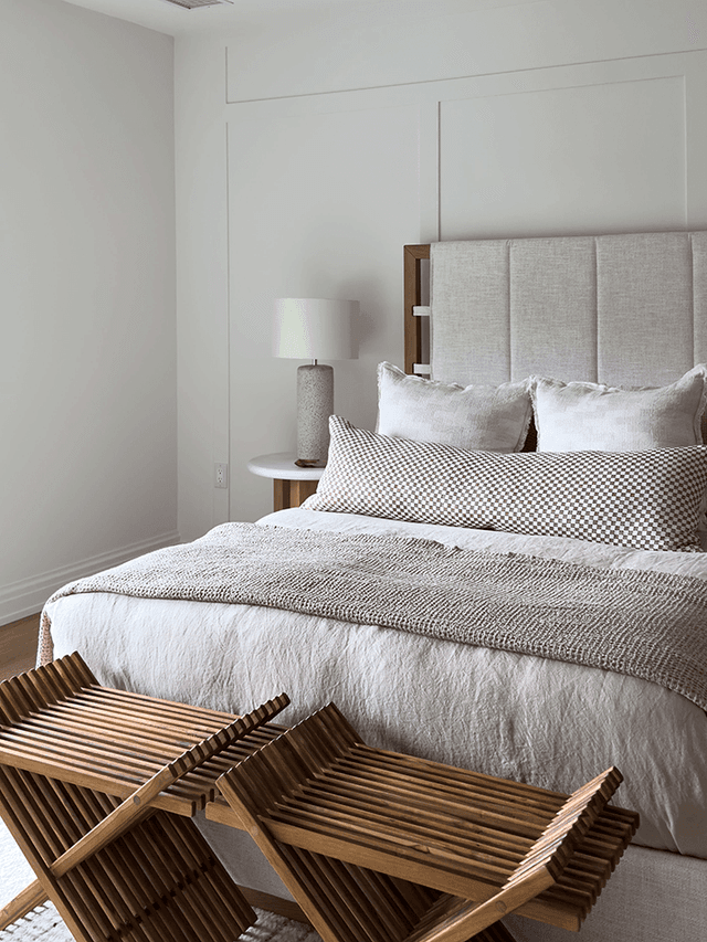 Guest room with an upholstered panel headboard, layered bedding and two slatted wooden benches at the foot of the bed