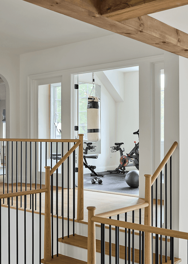 Landing beside the home gym of a Mendham, NJ home, with an oak handrail on black balusters and an exposed beam across the opening
