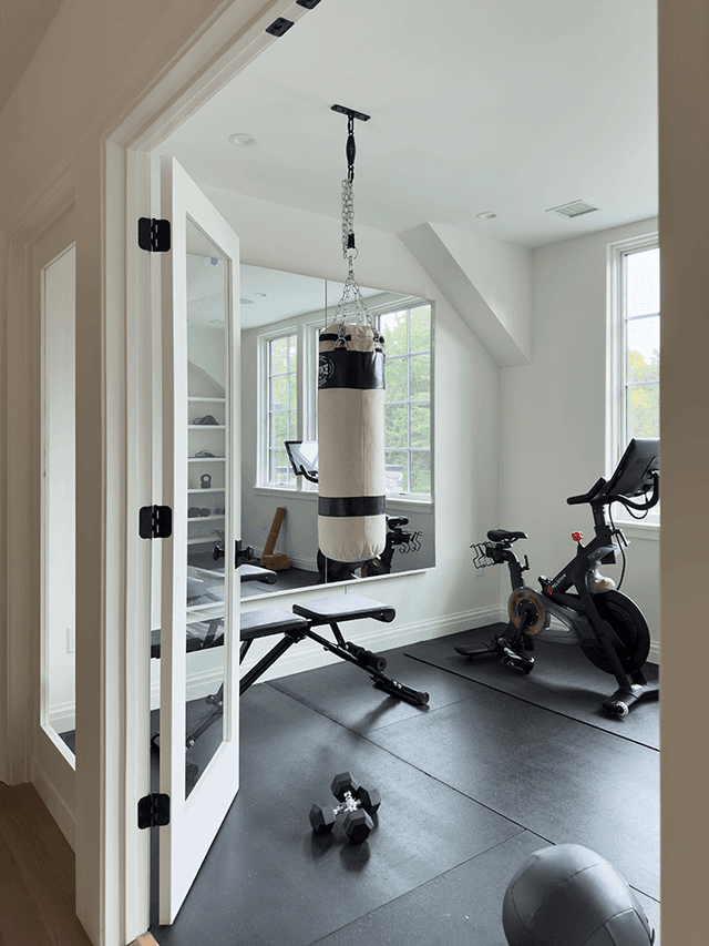 Home gym in a Mendham, NJ home seen through its steel-framed doors, with rubber flooring, a punching bag, two bikes and dumbbells