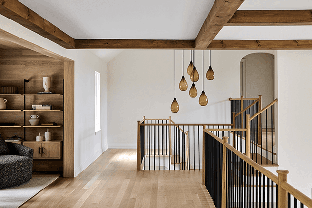 Upstairs hall of a Mendham, NJ home, with exposed beams, oak floors, a cluster of amber glass pendants over the stairwell and built-in shelving at the end