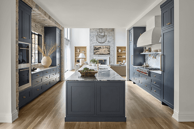 Marble-topped island and navy custom cabinetry in a Mendham, NJ kitchen, looking through the exposed stone wall to the family room fireplace