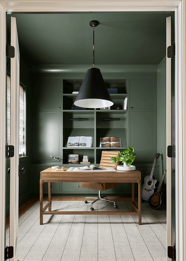 Home office in a Mendham, NJ home, painted deep green with built-in cabinetry, a black cone pendant and a guitar against the wall