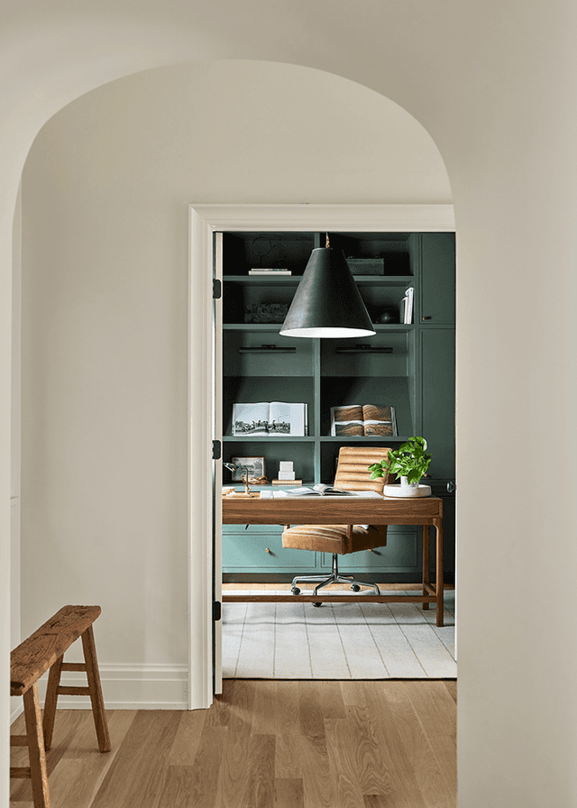 Arched doorway through to a home office in a Mendham, NJ renovation, with teal built-in cabinetry and a black cone pendant over the desk