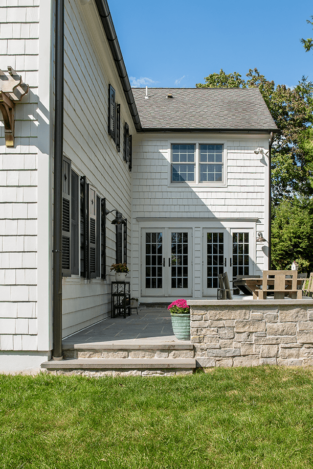 Raised stone patio and slate paving at the back of a Westfield, NJ exterior renovation, with gooseneck barn lights on the shingled wall above