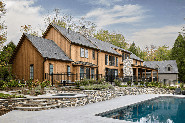 Pool and spa below the cedar and stone rear elevation of a Mendham, NJ home, with a dry-laid stone retaining wall between them